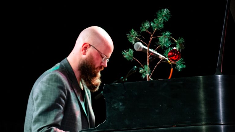 Anthony Deutsch of The Commercialists at the piano beside a Charlie Brown Christmas tree